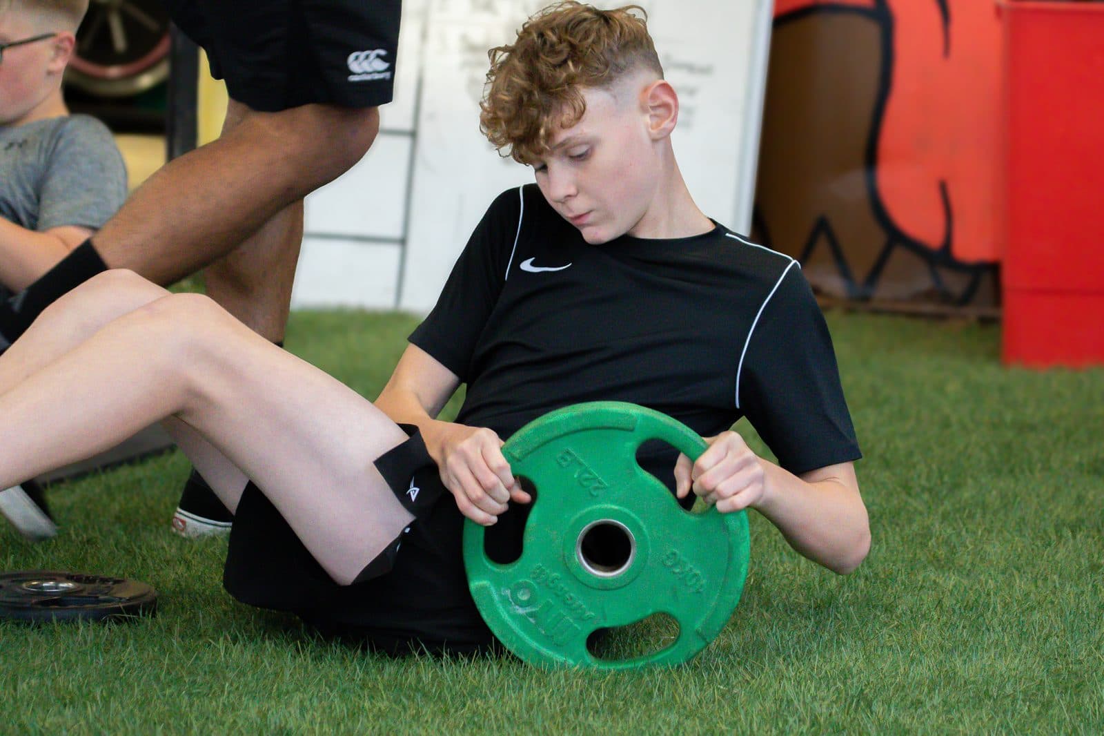 Young athletes doing seated core work with weight plates